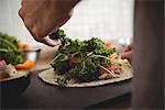 Close-up of mans hand placing herbs on burrito on kitchen worktop