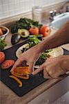 Close-up of mans hand slicing bell pepper on chopping board in the kitchen