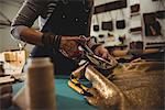 Mid-section of craftswoman cutting leather in workshop