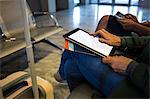 Mid-section of woman using digital tablet in waiting area at airport