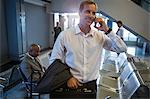 Businessman using his phone while near waiting area at airport terminal