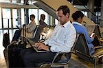 Man with luggage using laptop in waiting area at airport terminal
