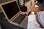 Man with laptop checking time while sitting at airport terminal