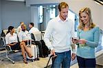 Couple standing with luggage holding Smartphone and boarding pass in waiting area