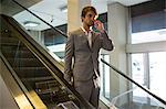 Businessman on escalator talking on mobile phone in airport