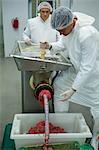Butchers using a meat mincing machine at meat factory