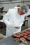 Male butcher maintaining records on clipboard at meat factory