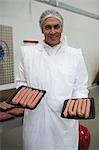 Portrait of butcher holding tray of meat sausages at meat factory