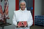 Portrait of butcher holding a meat tray at meat factory