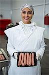 Portrait of female butcher holding tray of sausages at meat factory