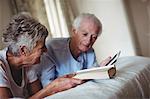Senior couple using digital tablet and reading book on bed in bedroom
