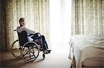 Senior man sitting on wheelchair in bedroom at home