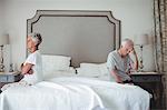 Senior man and woman sitting on bed and ignoring each other in bed room