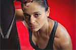 Portrait of tired female boxer leaning on punching bag in fitness studio