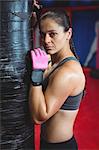 Portrait of tired female boxer leaning on punching bag in fitness studio