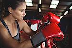 Thoughtful female boxer leaning on boxing ring in fitness studio