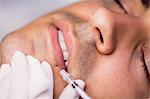 Man receiving botox injection on his lips at clinic