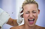 Close-up of scared woman shouting while receiving an injection from cosmetic treatment