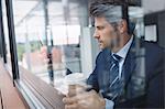 Businessman using mobile phone and holding disposable coffee cup in office