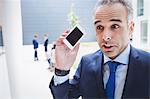 Businessman holding mobile phone and frowning outside office building