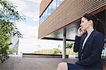 Businesswoman sitting outside office building and talking on mobile phone