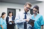 Doctor and nurse discussing over digital tablet in hospital corridor