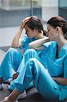 Sad nurses sitting on corridor in hospital