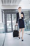 Businesswoman holding suitcase walking through office corridor