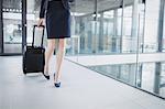 Low section of businesswoman holding suitcase walking through office corridor