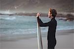 Side view of a man wearing wetsuit standing on beach with surfboard