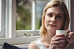 Thoughtful woman having coffee in living room at home