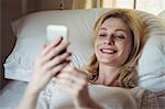 Beautiful woman lying on bed and using mobile phone in bedroom at home