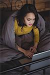 Woman lying on bed using laptop in bedroom at home