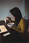 Woman eating cereal while working on laptop in study room at home