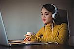 Woman listening to headphones while using laptop in study room at home