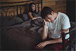 Upset couple ignoring each other after fight on bed in bedroom