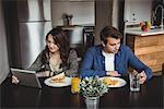 Couple using digital tablet and mobile phone while having breakfast at home