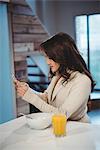 Woman using mobile phone while having breakfast at home