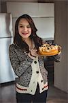 Cheerful woman holding blueberry cake in living room at home