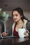 Woman having coffee while working on laptop at home