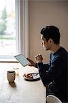 Man using digital tablet while having breakfast at home