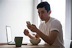 Man using mobile phone while having breakfast at home