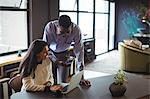 Businessman and a colleague discussing over laptop and mobile phone in office