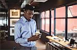 Businessman holding disposable coffee cup and using mobile phone in office