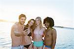 Young adult friends in bikinis and swim trunks taking selfie at summer sunset ocean