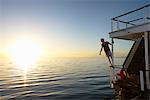 Man leaning on summer houseboat railing over sunset ocean