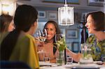 Smiling women friends toasting white wine glasses dining at restaurant table