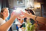 Smiling women friends toasting wine glasses dining at restaurant table