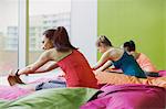 Women stretching legs in forward fold pose on cushions in restorative yoga gym studio