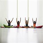 Women on cushions with arms raised in restorative yoga gym studio